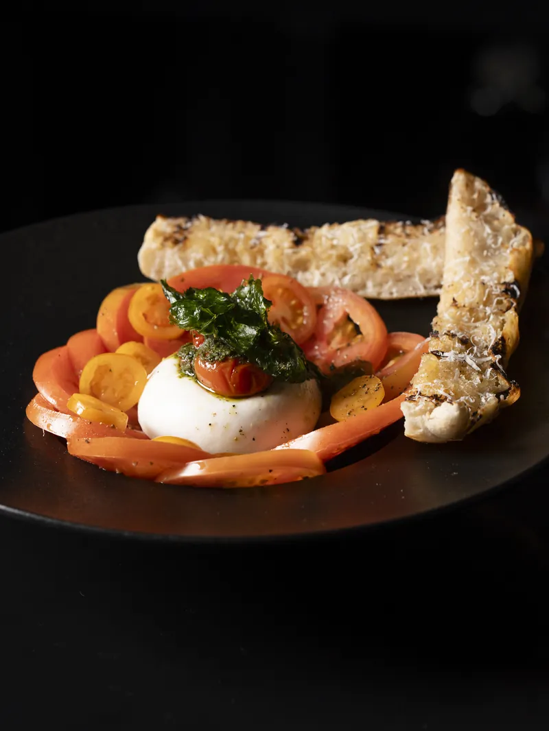Burrata with tomatoes and grilled bread on a black plate