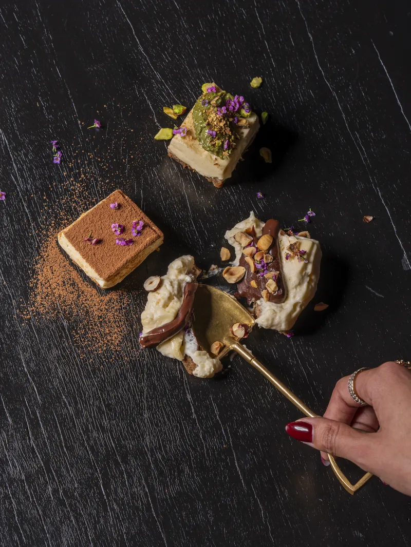 Dessert squares on a dark surface, with a gold spoon