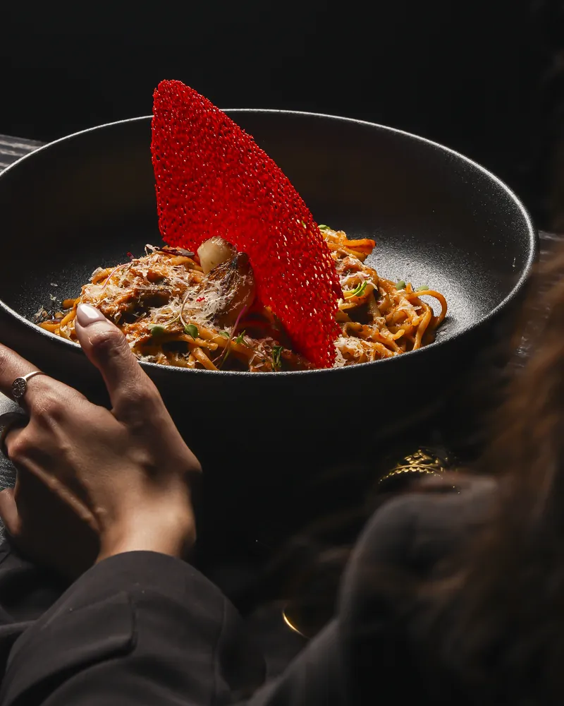 A bowl of pasta topped with a red tuile